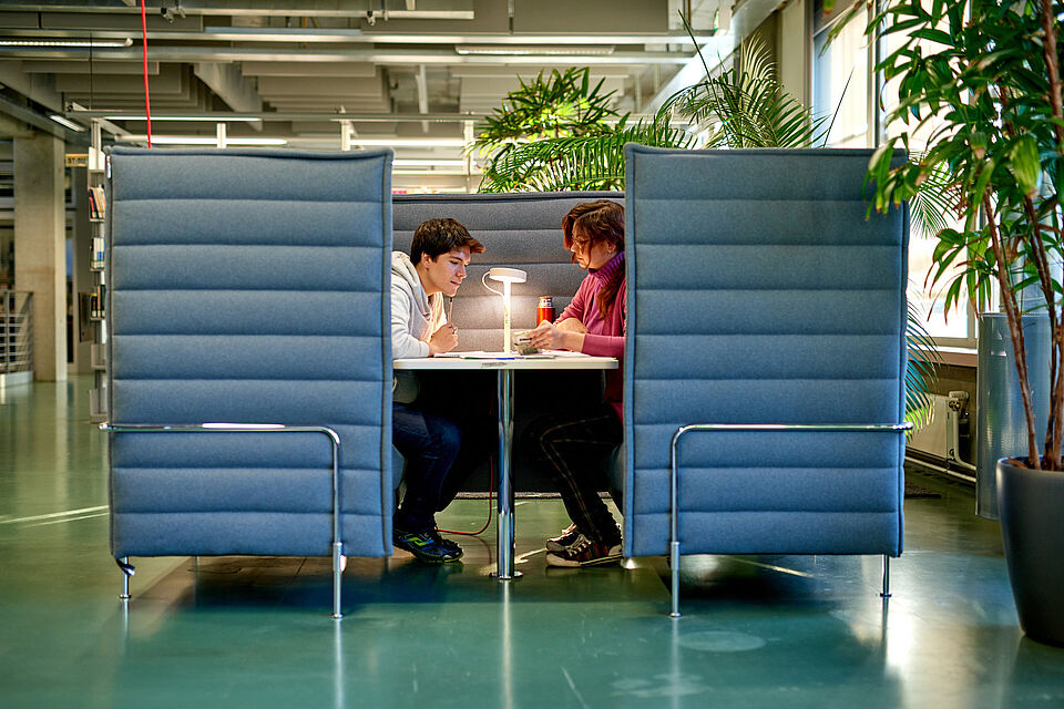 Zwei Studierende sitzen in einer Workbay. Das ist ein quadratisches, offenes Möbel zur Gruppenarbeit.