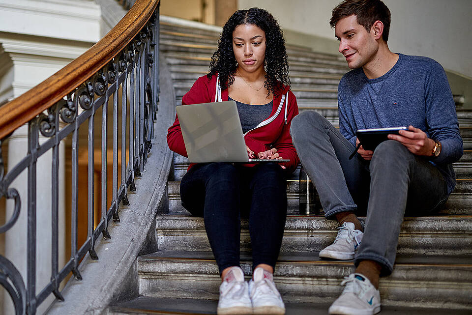 Studierende mit Laptop auf einer Treppe im Hauptgebäude