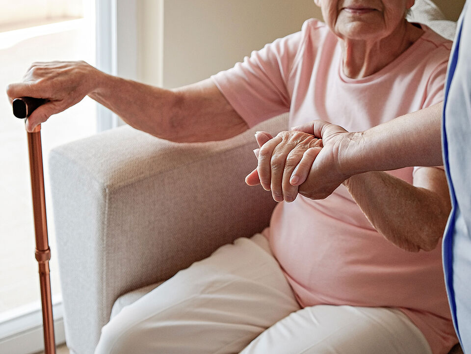 close up on hands of an sitting elderly woman and a younger standing woman, the elderly woman has a walking stick in her other hand