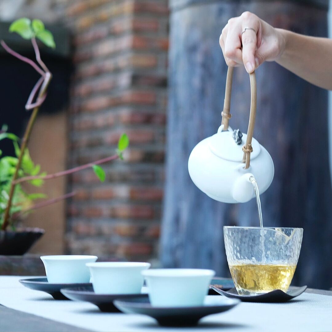 Tee wird aus einer weißen Teekanne in ein Gefäß gegossen