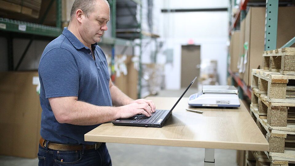 Mann in einem Lager stehend bei der Arbeit an einem Laptop