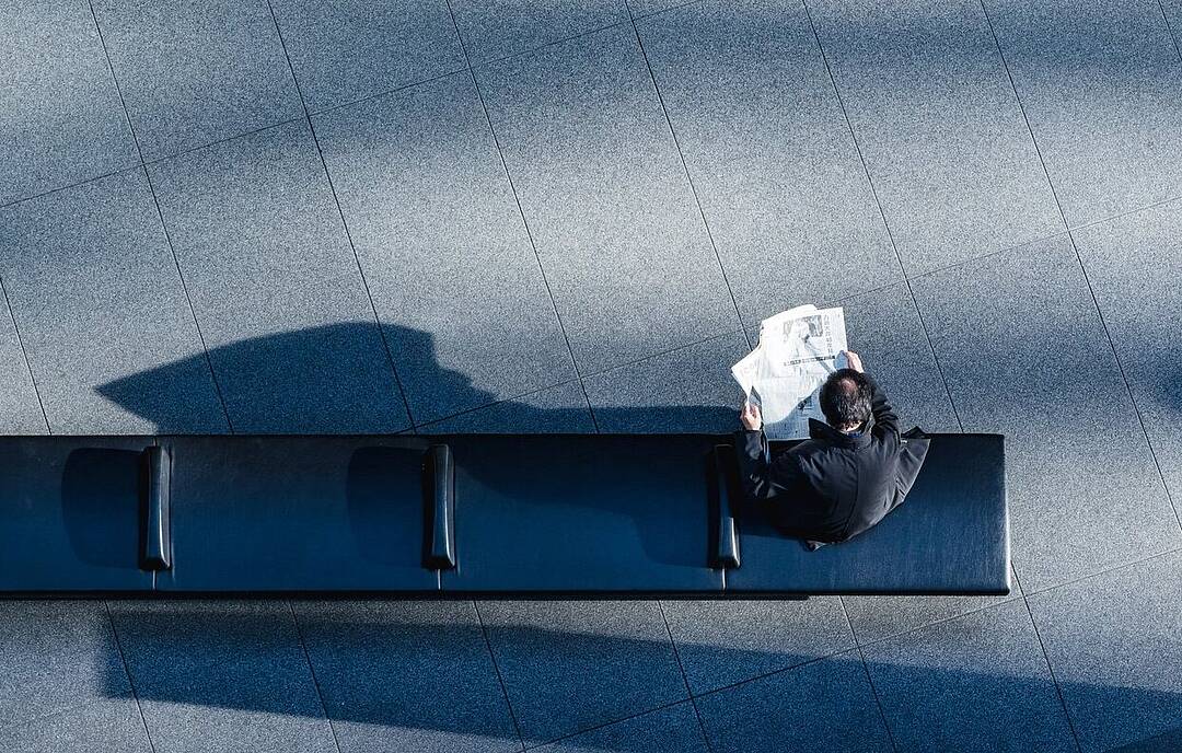 Bird's eye view: Person sitting on a black bench, reading a newspaper