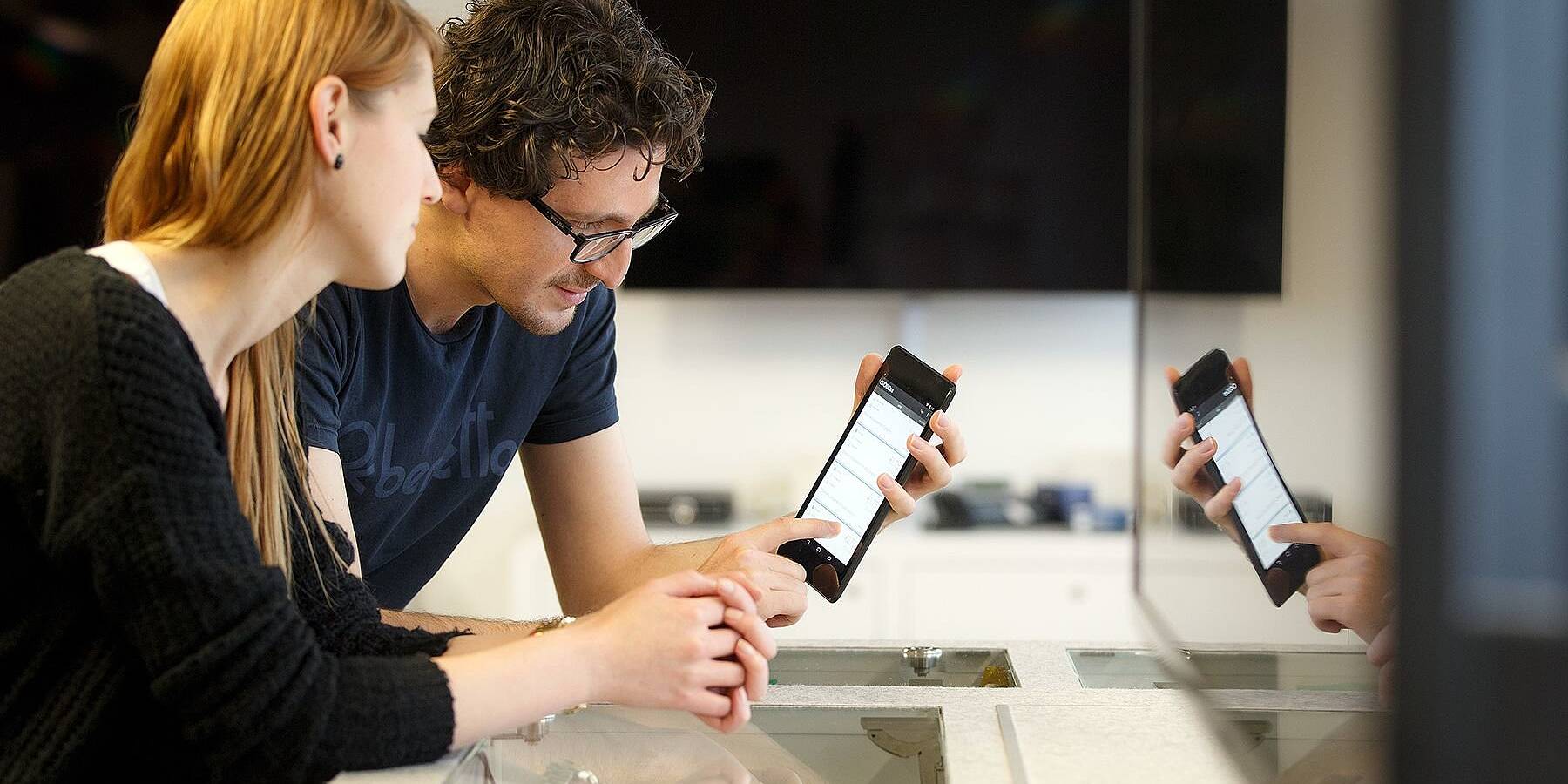 Zwei Personen in einer Werkstatt ein Smartphone in der Hand und Daten darauf betrachtend
