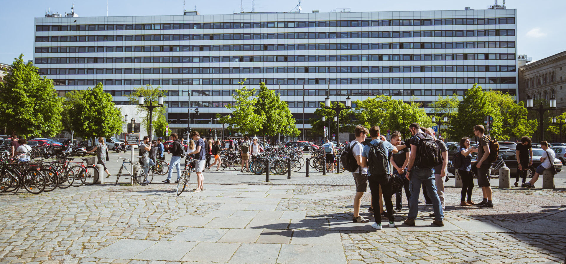 View of TU Berlins main building across Straße des 17. Juni in sunshine, students are standing in groups