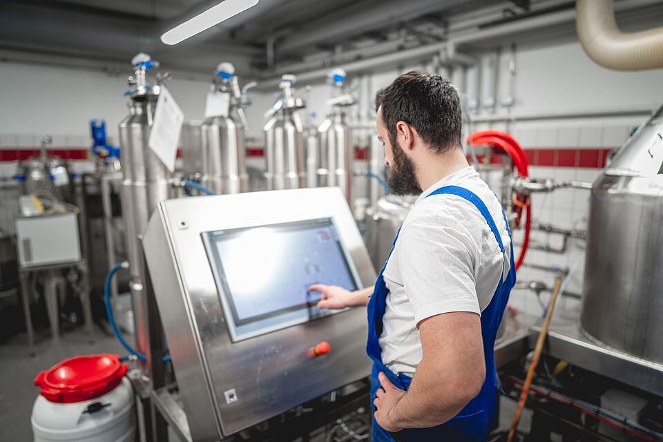 A trainee stands with his back to a device in the research brewery of the TU Berlin and presses a button