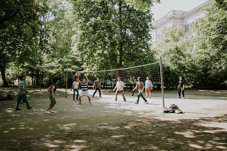 Mehrere Studierende spielen Volleyball auf dem Volleyballfeld auf der Rückseite des Hauptgebäudes am Hauptcampus
