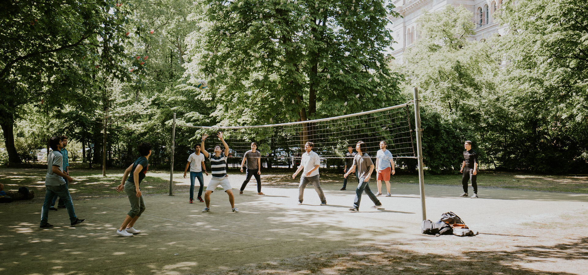 Mehrere Studierende spielen Volleyball auf dem Volleyballfeld auf der Rückseite des Hauptgebäudes am Hauptcampus