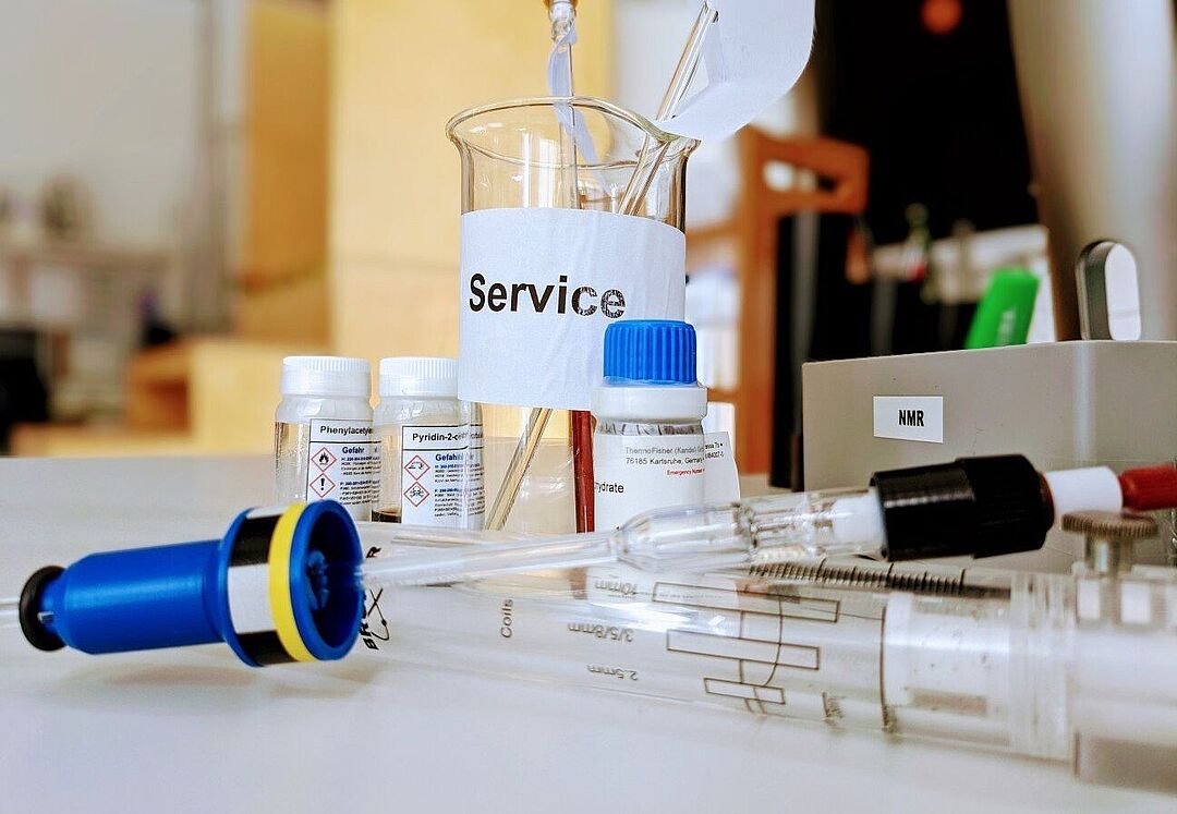 Servicebecherglas mit NMR-Röhrchen, davor 3 Chemikaliengefäße, Kalibrierlehre mit Spinner und High-Pressure-Röhrchen