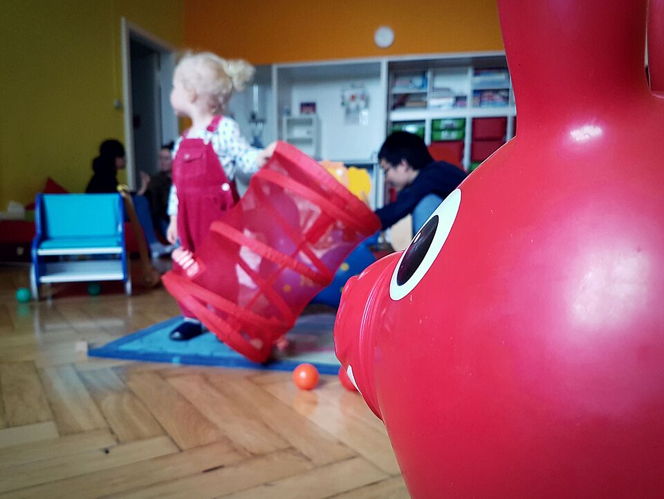 in the foreground you can see a part of a toy, in the background you can see a blurred child playing in a family room of the TU berlin