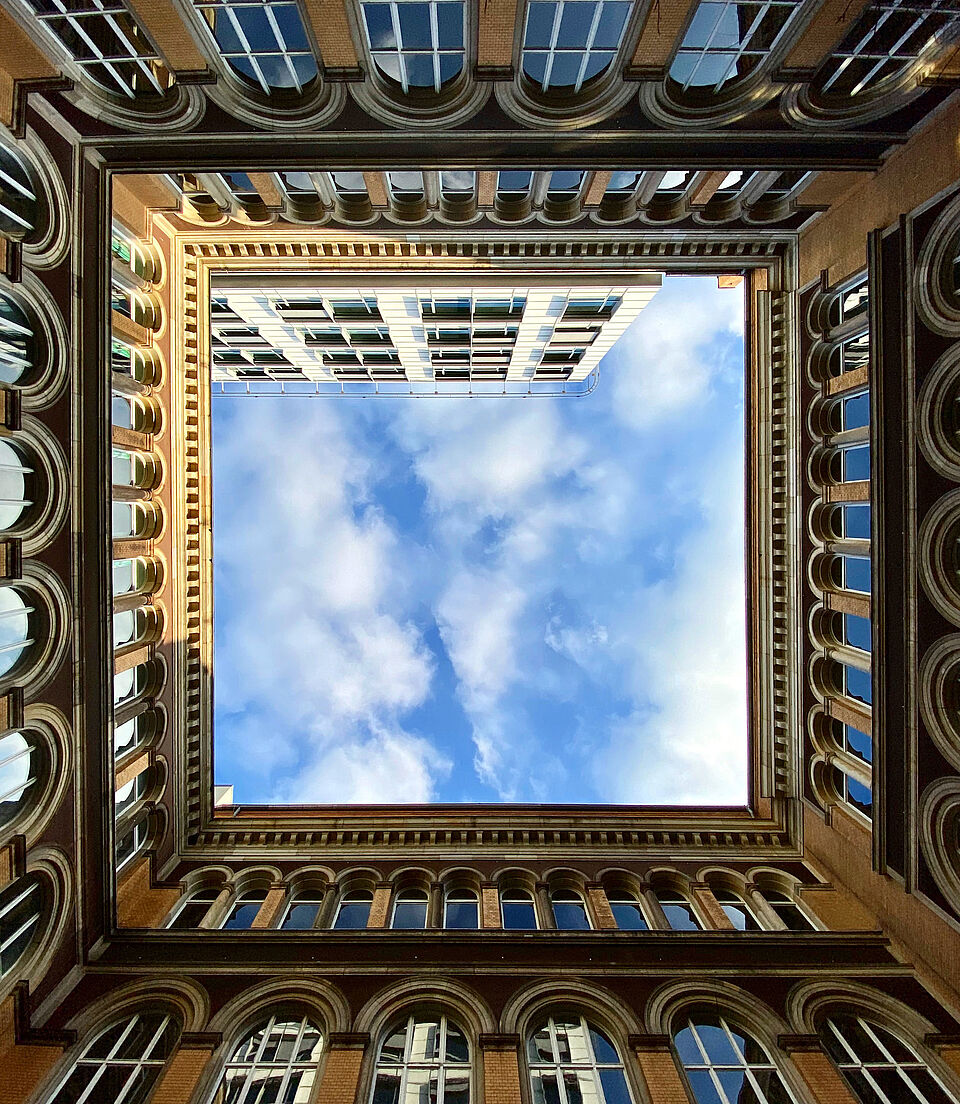 Blick in den Himmel im Innenhof des Hauptgebäudes, die Fassade des Gebäudes bildet einen Rahmen um den Himmel