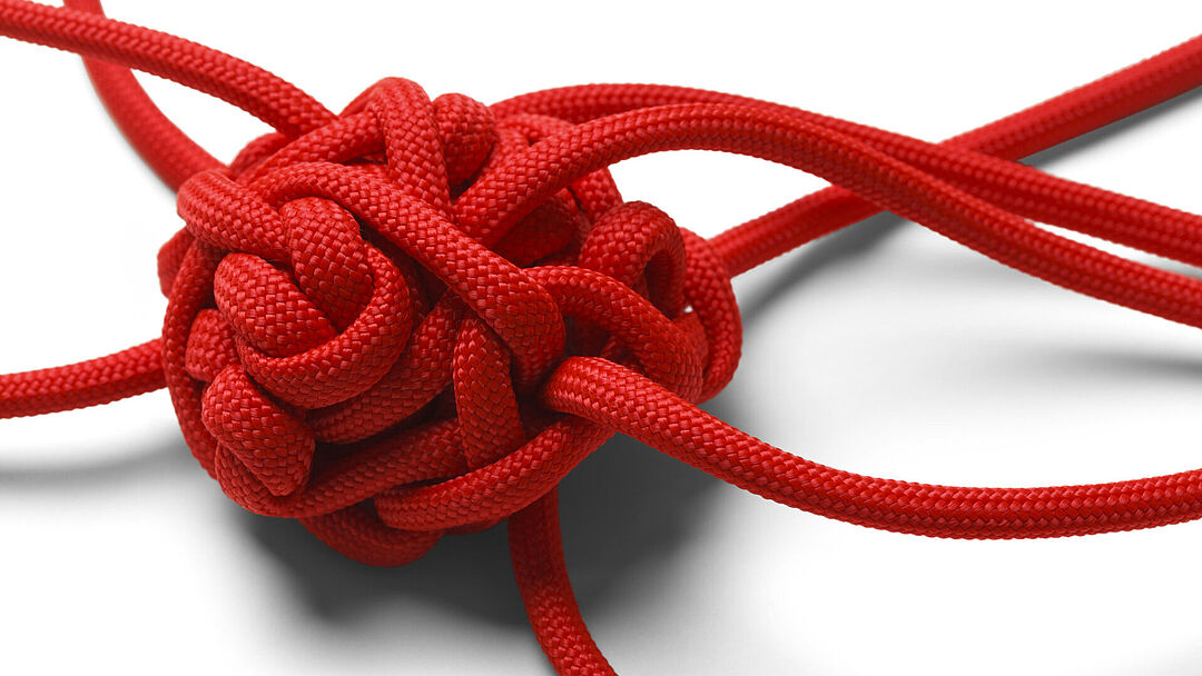 Knoten-Wirrwarr aus einem roten Seil auf weißem Hintergrund