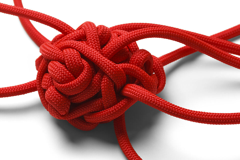 Knoten-Wirrwarr aus einem roten Seil auf weißem Hintergrund