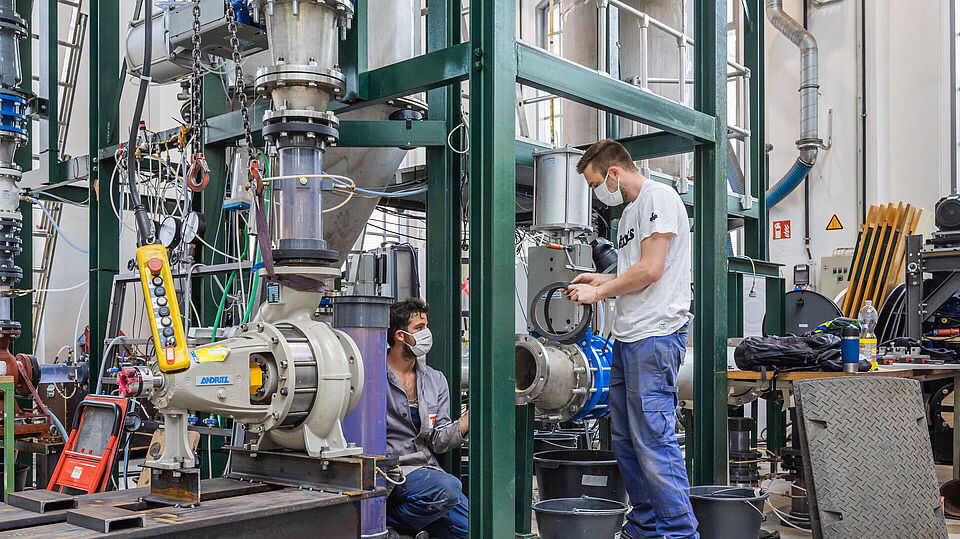 Zwei männliche Studierende arbeiten an ihren Projekten in der Versuchshalle K des Fachgebietes Fluidsystemdynamik