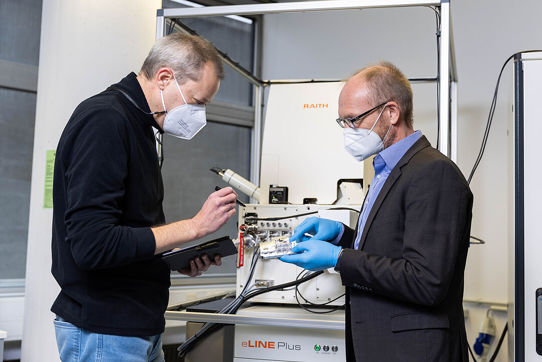 Head researcher Sven Rodt (left) and Stephan Reitzenstein in front of their lithography system - the only one of its kind in the world. It uses an electron beam to write nanometer-sized structures into a semiconductor material in which the quantum dot molecules are embedded. The specimen holder used for this purpose may only be touched wearing gloves.
