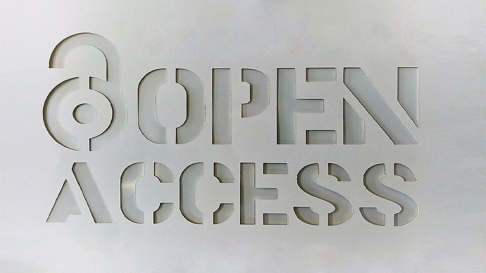 Das Bild zeigt eine weiße Schablone mit dem Schriftzug 'Open Access'. Links in der Ecke ist ein geöffnetes Vorhangeschloss (das offizielle Zeichen für Open Access) zu sehen.