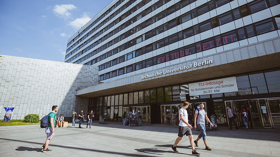 Haupteingang mit angeschnittenem Audimax und Hauptgebäude, Studierende betreten und verlassen das Gebäude