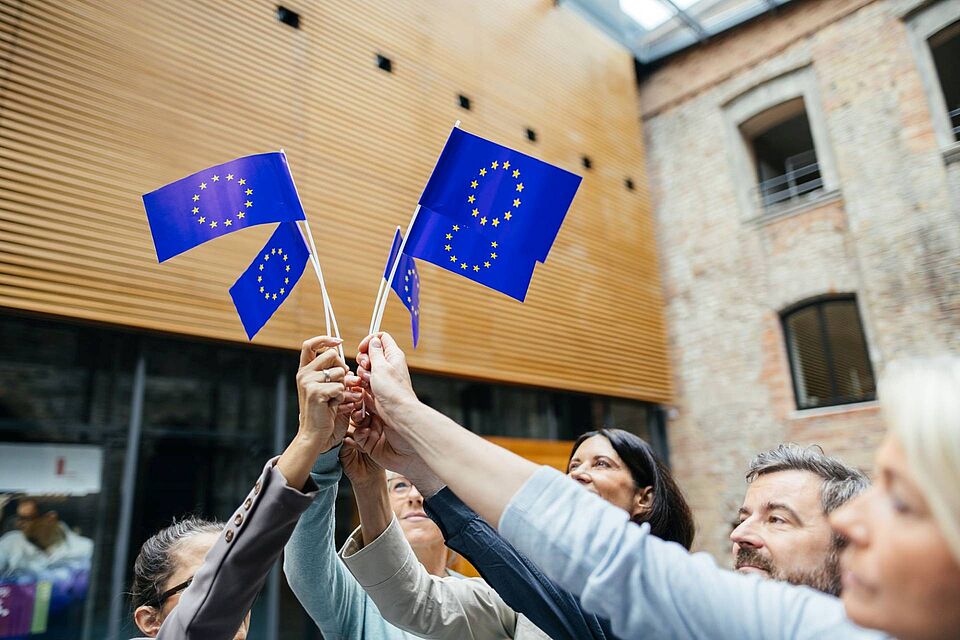 Hochschulvertreter:innen halten Fähnchen mit der Europaflagge in die Luft