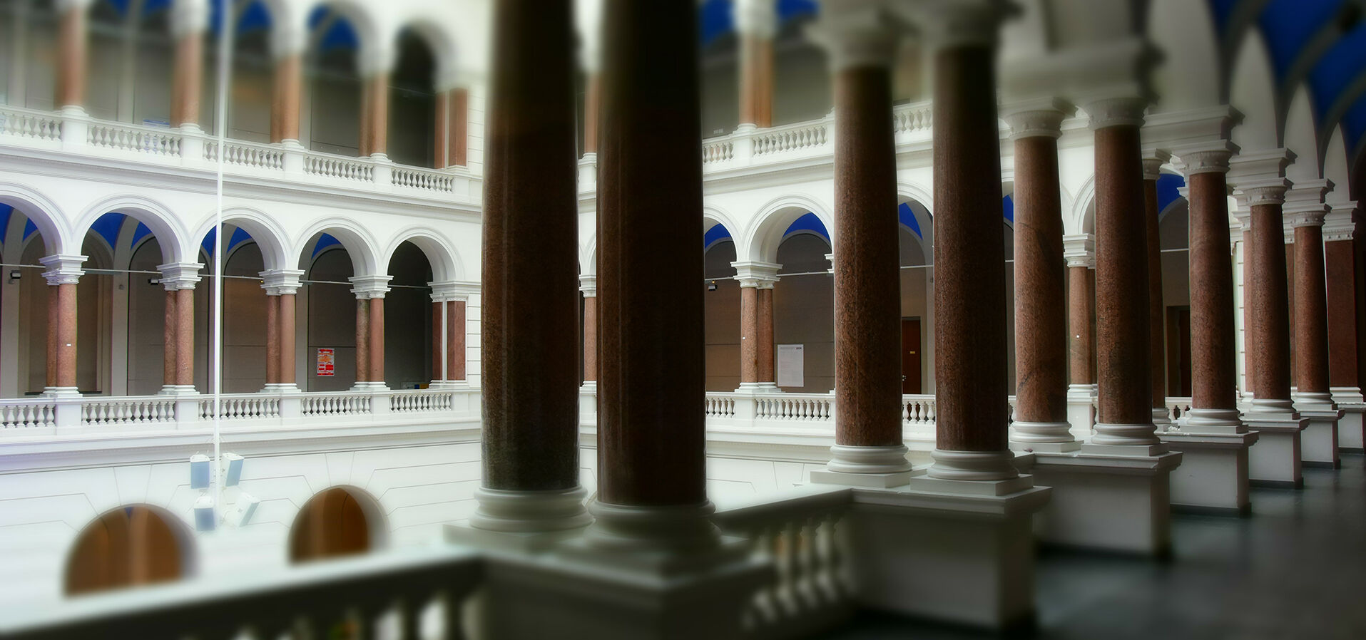Lichthof über drei Etagen mit umlaufenden Säulengängen aus roten Granitsäulen mit weißem Abschluss oben und unten, Gangdecke blau gestrichen