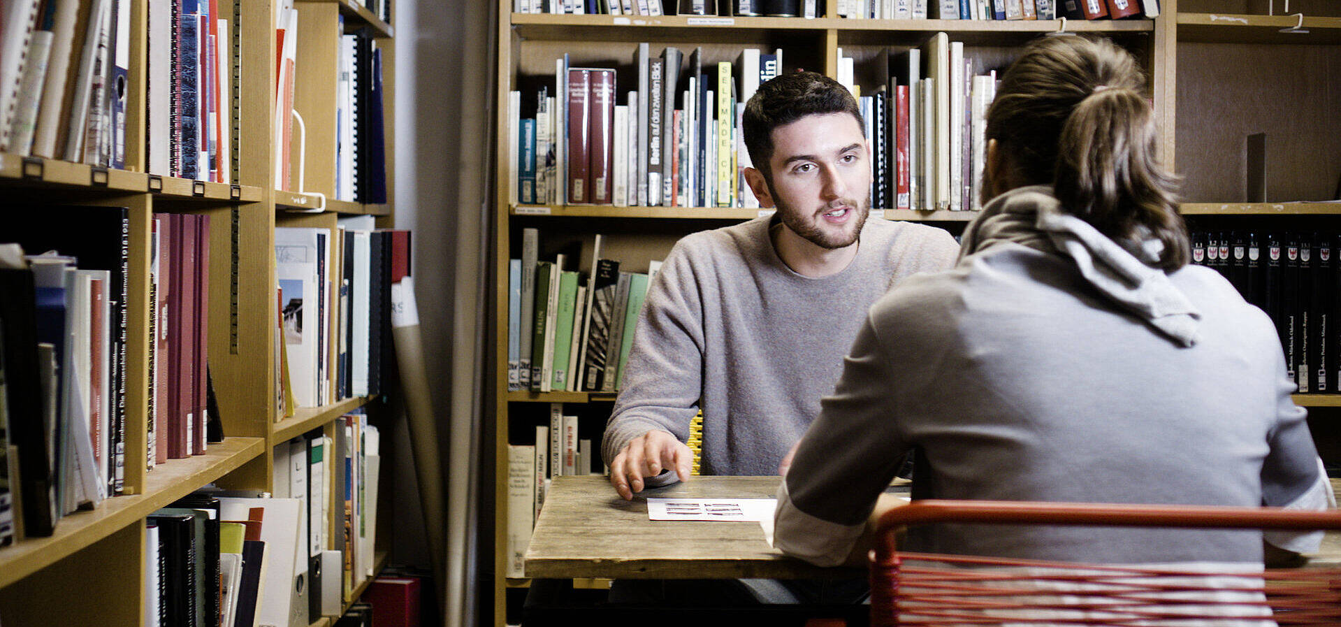 Zwei Studierende sitzend bei einem Gespräch in der Universitätsbibliothek