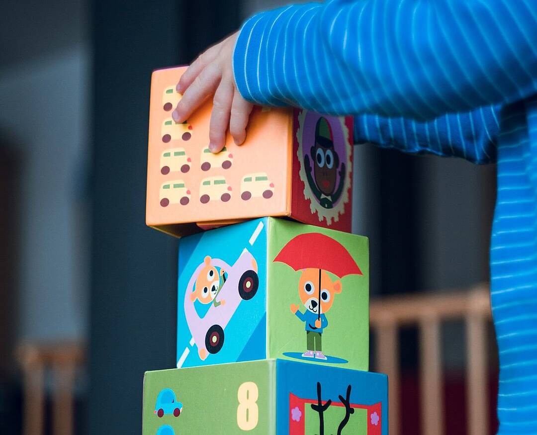 Symbolbild: Kind baut einen Turm aus Bauklötzen (Würfel) mit Tiermotiven