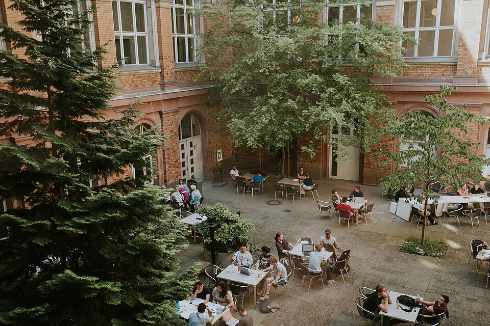 Studierende sitzen an Tischen im Innenhof des Hauptgebäudes bei schönen Wetter
