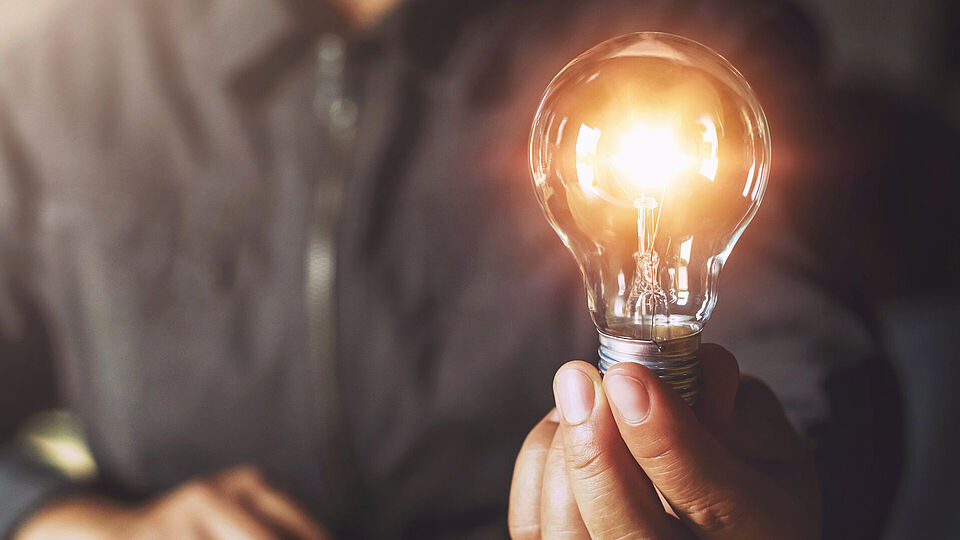 Hand, die eine Glühbirne hält. Ideenkonzept mit Innovation und Inspiration.