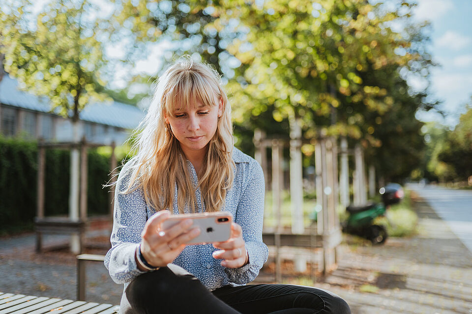 Studierende mit einem Smartphone auf einer Bank sitzend