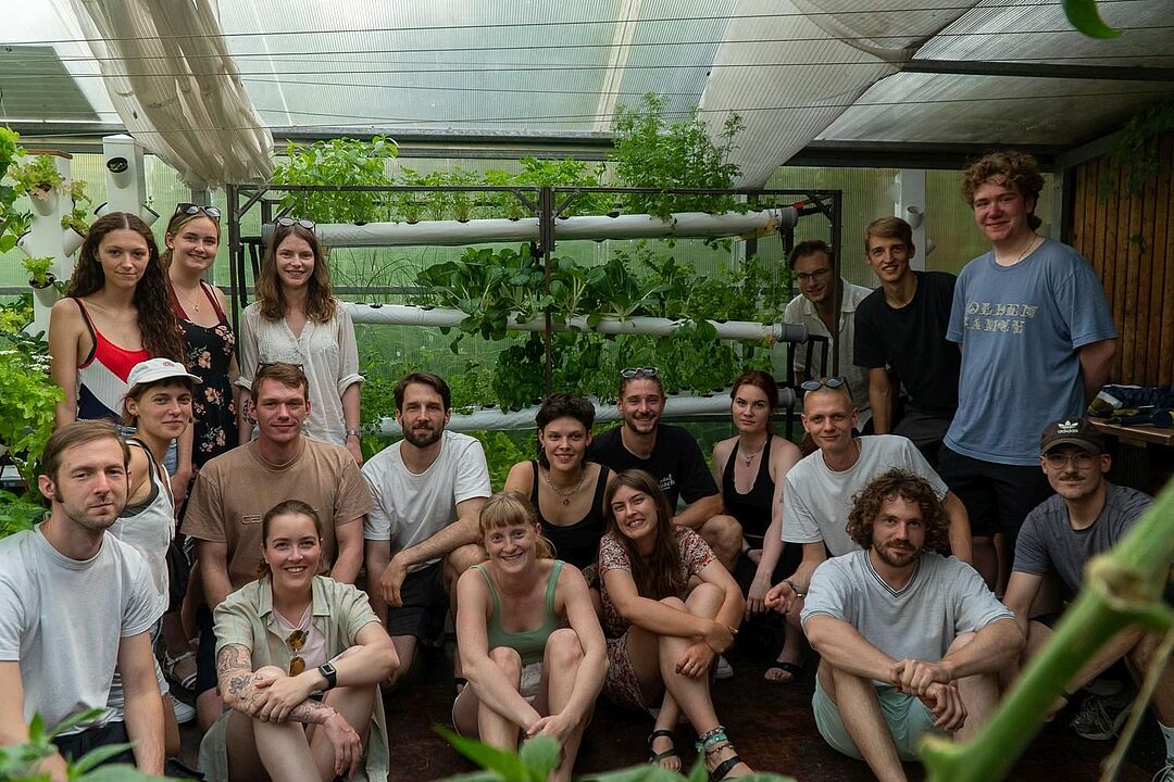 Teamfoto mit insgesamt 19 Personen, im Hintergrund der Hydroponik-Prototyp, in dem verschiedene Salate und Kräuter wachsen.