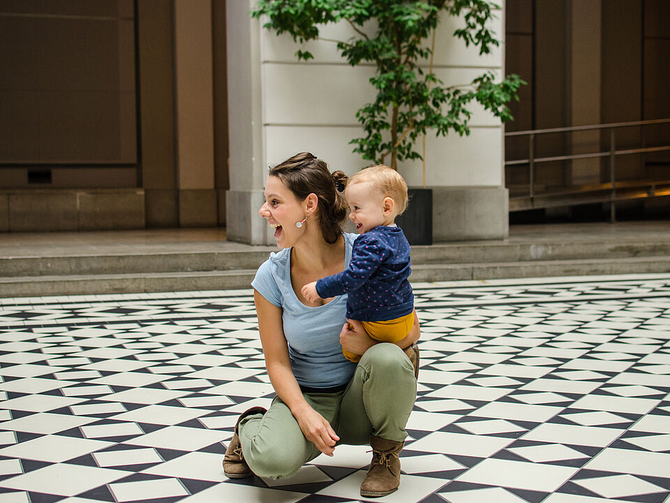young woman kneeling with child on lap in atrium, both laughing