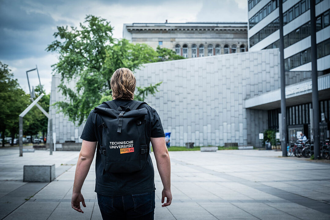 Studierender vor dem Hauptgebäude der Technischen Universität Berlin mit einem Rucksack aus dem Uni-Shop