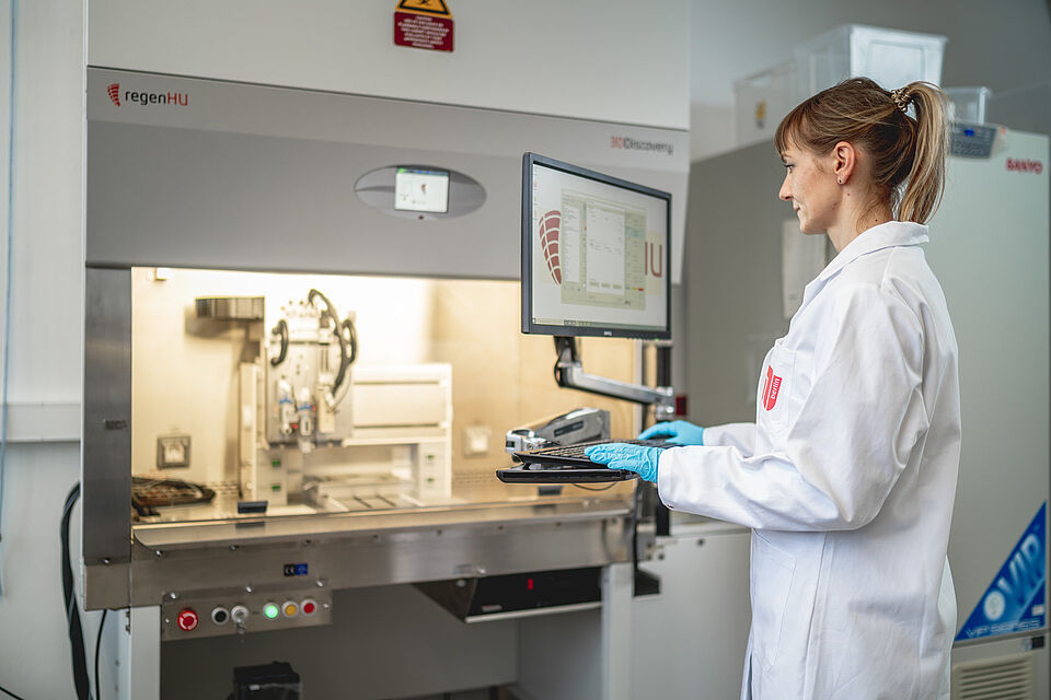 A young scientist stands at a monitor in a laboratory of the Chair of Applied Biochemistry and looks at a screen, behind which laboratory equipment