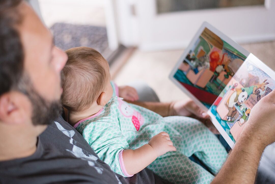 Vater mit Baby auf dem Schoß ein Bilderbuch betrachtend