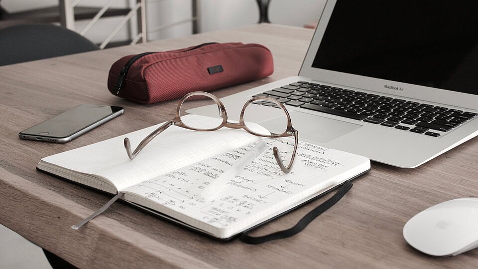 Schreibtisch mit einem Laptop, einem Notizbuch mit Brille darauf