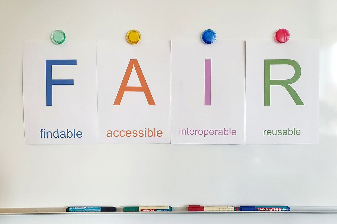 Auf einem Whiteboard steht in bunten Buchstaben FAIR. Darunter steht findable, accessible, interoperable und resuable.