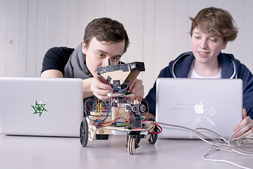 2 Studierende mit Laptops und rollendem Roboterentwurf