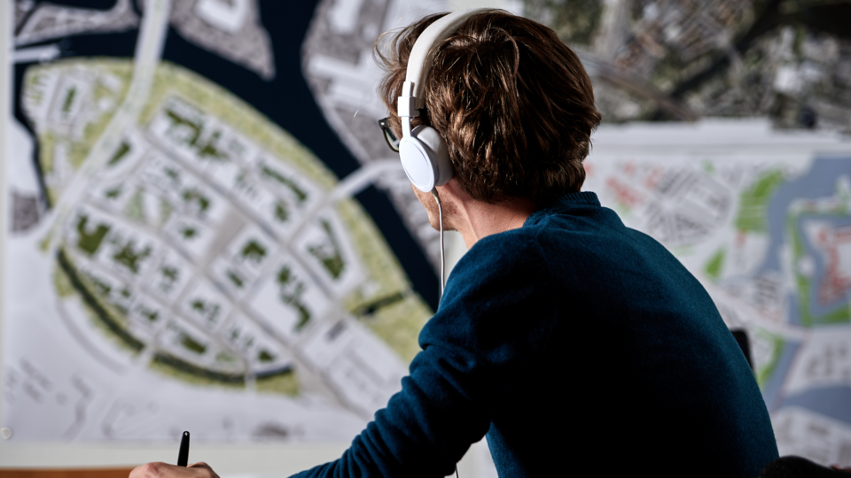 junger Mann mit Kopfhörern blickt auf einen Stadtplanausschnitt an der Wand
