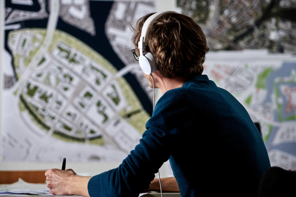 junger Mann mit Kopfhörern blickt auf einen Stadtplanausschnitt an der Wand