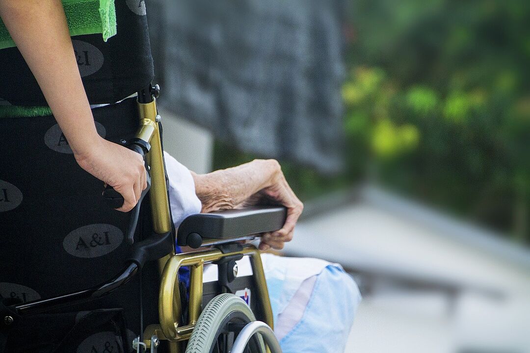 Älterer Mensch im Rollstuhl geschoben von hinten