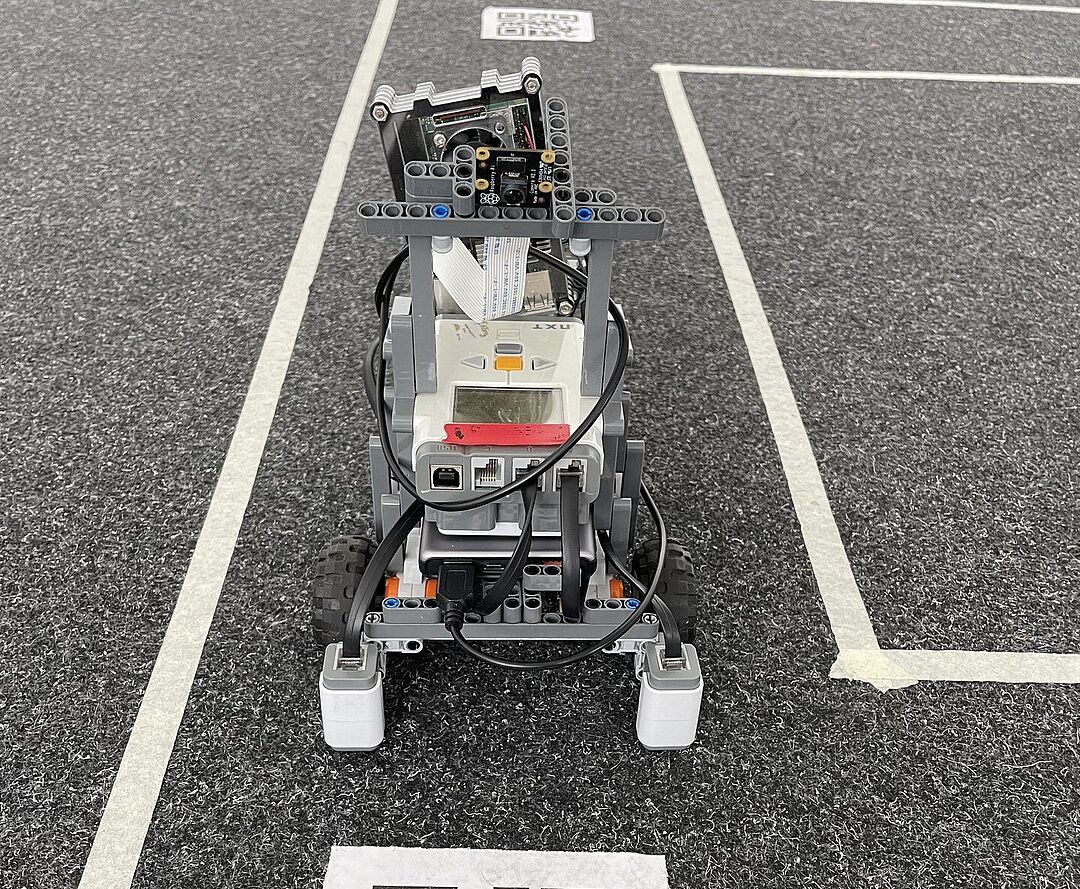 Ein Roboter, der sich auf einer Fahrbahn befindet und vor einem QR Code hält.