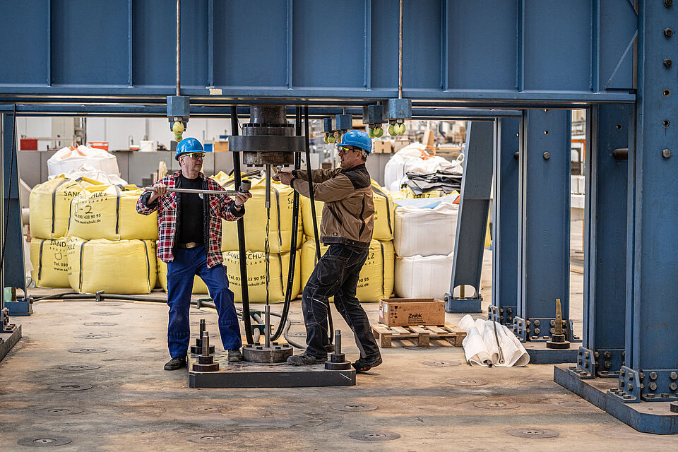Zwei Beschäftigte bei der gemeinsamen Arbeit an einer Maschine in der Peter-Behrens-Halle auf dem TIB-Gelände