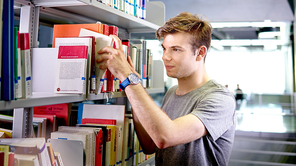 Student nimmt ein Buch aus dem Regal