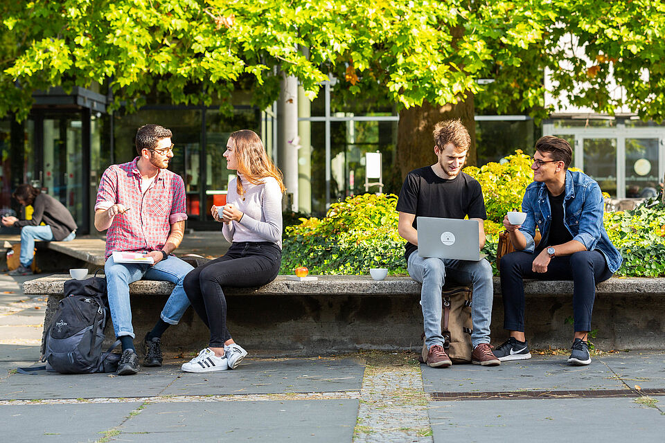 Studierende der Technischen Universität Berlin auf dem Campus sitzen und erzählend