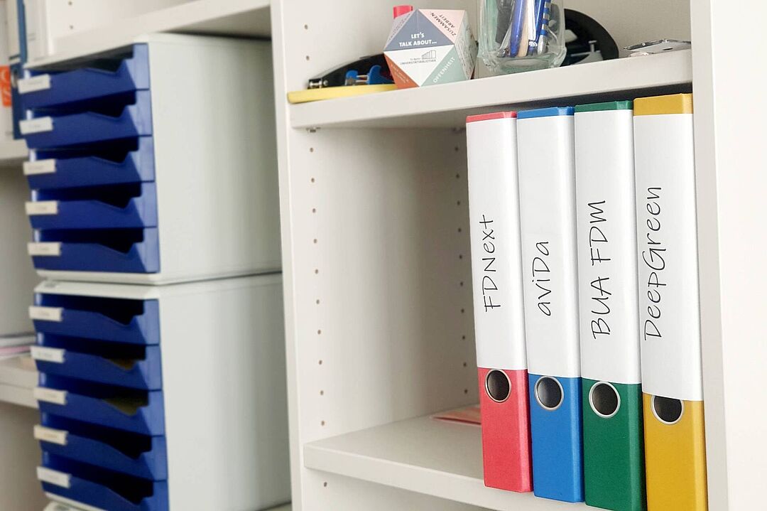 An office shelf with folders on which the acronyms of the funded projects are written