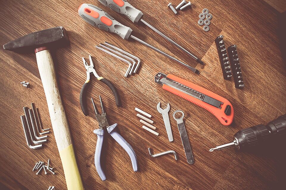 Handwerkzeuge, wie Hammer, Zange und Schraubendreher, liegen auf einem Tisch