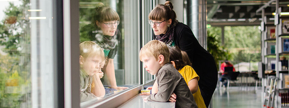 3 children and a caregiver are standing at the window of the university library of the TU Berlin and looking out of the window