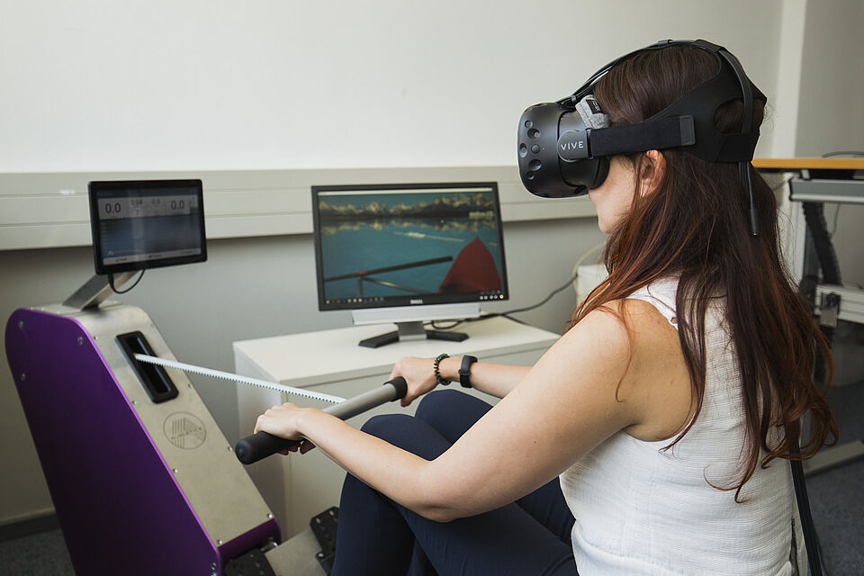 Studierende des Studiengangs Medieninformatik mit einer VR-Brille auf einem Rudergerät